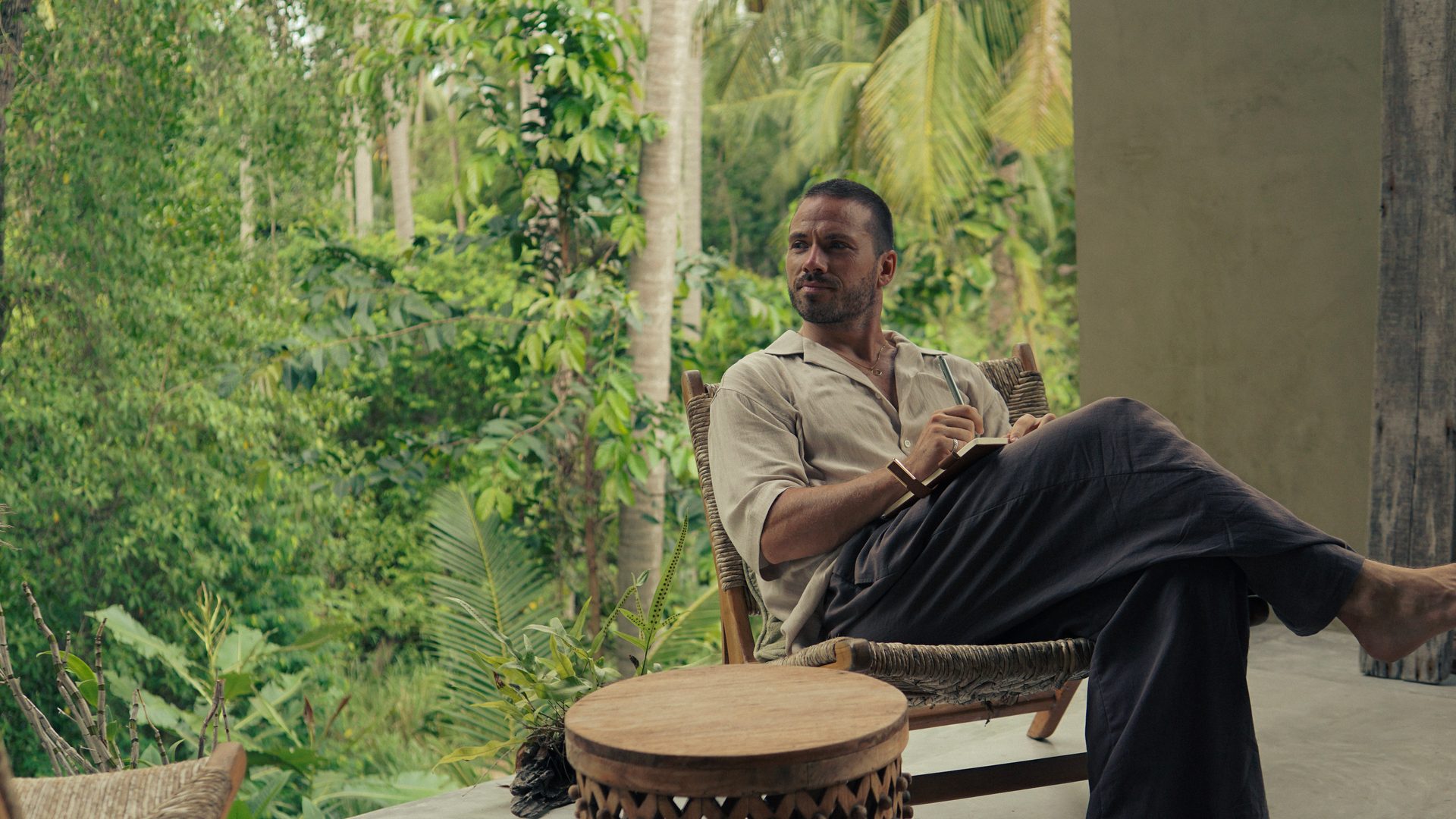 Axel Bjerkland, founder of Humain Communications, sitting with a notebook on an open terrace surrounded by jungle.